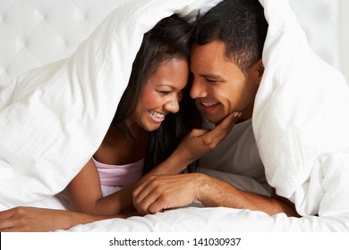 Couple Relaxing In Bed Hiding Under Duvet