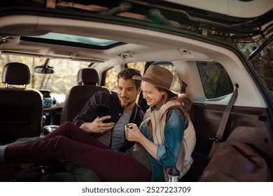 Couple relaxing in car trunk while reviewing photos on camera during road trip - Powered by Shutterstock