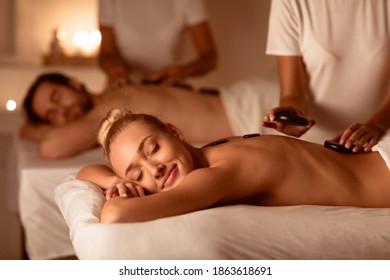 Couple Relaxing Enjoying Exotic Hot Stones Massage Lying On Beds In Luxurious Spa Center. Relaxation Beauty Treatment, Body Care, Wellness Concept. Low Light, Selective Focus - Powered by Shutterstock