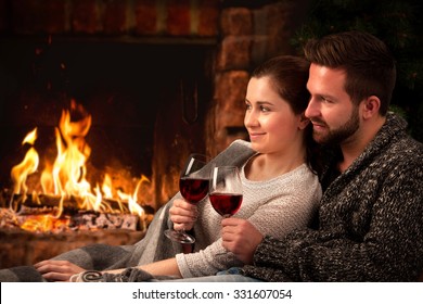 Couple Relaxing With Glasses Of Red Wine At Romantic Fireplace On Winter Evening