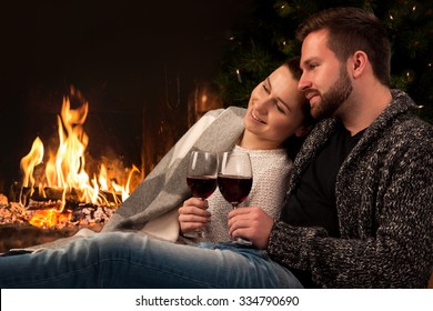 Couple relaxing with glasses of wine at romantic fireplace on winter evening