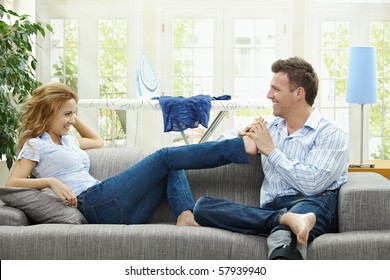 Couple Relaxing At Home On Sofa, Man Giving Foot Massage To Her Gildfriend.