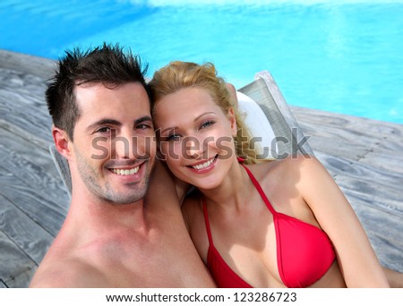 Couple relaxing in long chairs by swimming-pool