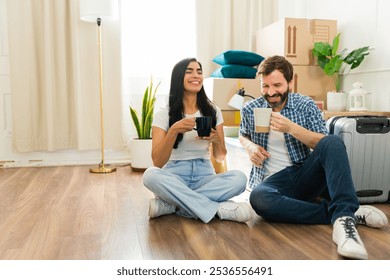 Couple is relaxing on the floor of their new home, drinking coffee and enjoying a moment of peace during the stressful moving process - Powered by Shutterstock