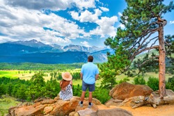 Couple Relaxing On Hiking Trip In The Beautiful Park. Man And Woman Sitting Looking At Summer Mountain View. Friends Enjoying Nature. Rocky Mountain National Park, Estes Park, Colorado, USA.