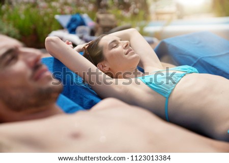 Couple relaxing on longchairs at resort pool