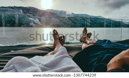 Couple relaxing on the sun beds in Spa, Badehaus Millstätter See, Austria, by Millstätter See. Only the legs are visible and some parts of bathrobes. Snowy mountains in the back, snow on the terrace