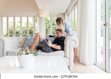 Couple Relaxing Together On Sofa With Laptop Computer In Luxury Villa