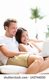 Couple relaxing together in sofa with laptop pc computer having fun. Romantic young happy multiracial couple lying at home in sofa resting having fun together maybe watching movie. Man and woman.