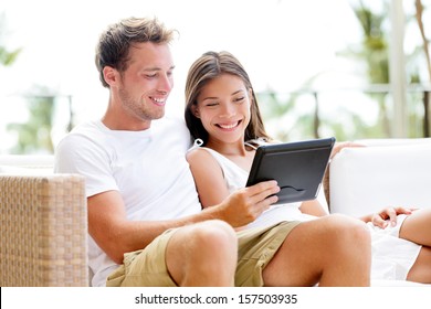 Couple relaxing together in sofa with tablet computer pc having fun. Romantic young happy multiracial couple in love sitting at home in sofa resting having fun maybe watching movie. Man and woman. - Powered by Shutterstock
