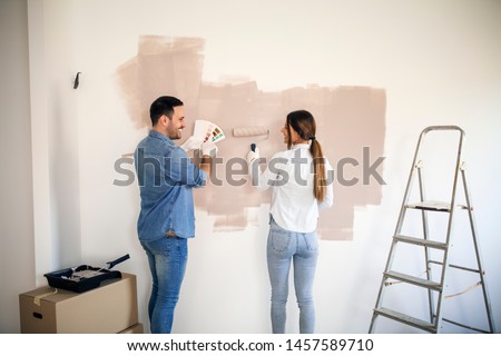 Couple renovating their apartment while man holding color palette and woman painting walls with roller. Imagine de stoc © 
