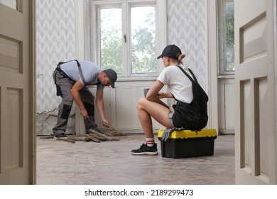 Couple Renovating Their Own Apartment. Home Improvement And DIY Project. Young Couple Is Removing Old Wooden Floor, Making Repairs To Their Home