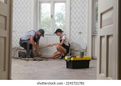 Couple Renovating Their Own Apartment. Home Improvement And DIY Project. Young Couple Is Removing Old Wooden Floor, Making Repairs To Their Home	