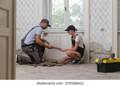 Couple Renovating Their Own Apartment. Home Improvement And DIY Project. Young Couple Is Removing Old Wooden Floor, Making Repairs To Their Home	