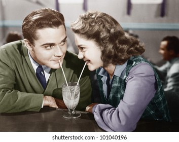 Couple in a restaurant looking at each other and sharing a milk shake with two straws