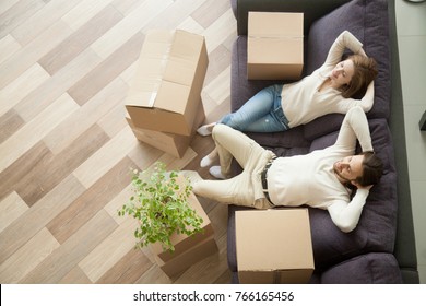 Couple resting on couch after moving in, man and woman relaxing on sofa just moved into apartment with cardboard boxes on floor, happy satisfied homeowners enjoying first day in new home, top view - Shutterstock ID 766165456