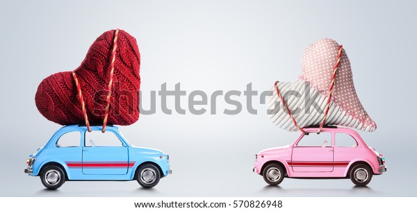 Couple of retro toy cars delivering craft\
hearts for Valentine\'s day on gray\
background