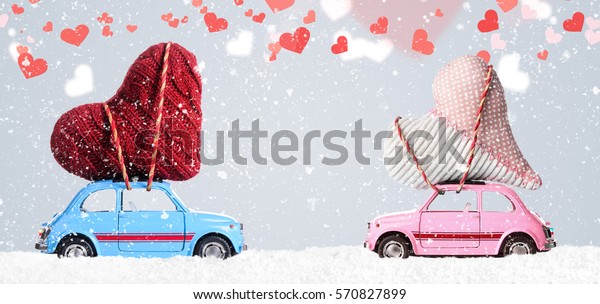 Couple of retro toy\
cars delivering craft hearts for Valentine\'s day on gray background\
with flying hearts