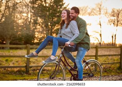 Couple Riding Bike Through Countryside With Woman Sitting On Handlebars - Powered by Shutterstock