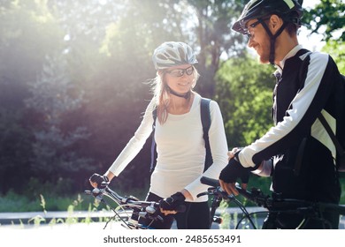 Couple riding bikes. Cyclists in protective bicycle helmets in park. Concept of safety, healthcare, ecological lifestyle. Outdoor sports activity in nature. Man showing navigation, time on smartwatch - Powered by Shutterstock