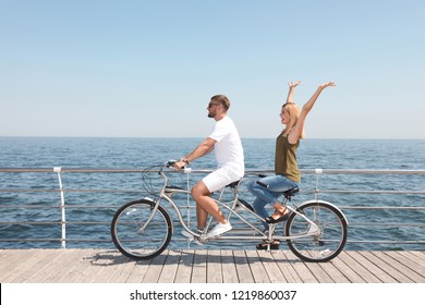 Couple Riding Tandem Bike Near Sea On Sunny Day