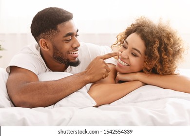 Couple romance. Playful african man flirting with wife, touching her nose in bed