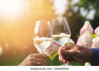 Couple Romantically Celebrate Outdoors With Glasses Of White Wine, Proclaim Toast People Having Dinner In A Home Garden In Summer Sunlight.