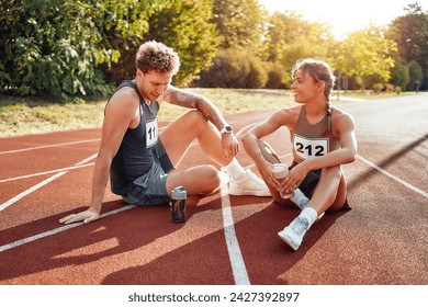 A couple of runners in sportswear with numbers resting after a run at the stadium. Morning exercises and jogging. Sports and  active lifestyle. - Powered by Shutterstock