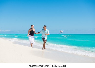 Couple Running At The Seashore Of Caribbean Sea In Cancun, Mexico. They Are Laughing And Happy.