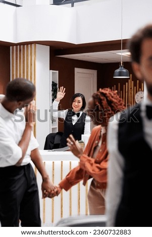 Couple saying goodbye to hotel employee, front desk staff waving at tourists after staying at modern resort with luxury service. Young guests checking out of room, accommodation service.