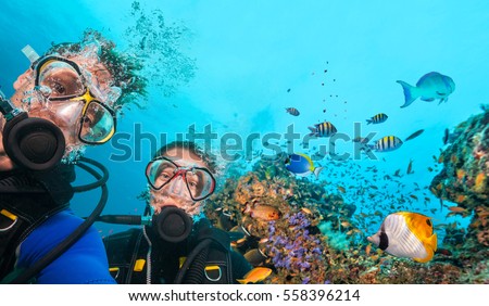 Couple of scuba divers looking at camera underwater. Beautiful coral reef with many fish on background