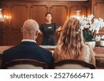 A couple is seated facing a wedding officiant during a simple indoor ceremony. The man has a bald head.