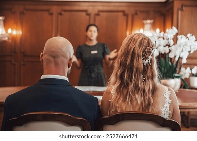 A couple is seated facing a wedding officiant during a simple indoor ceremony. The man has a bald head. - Powered by Shutterstock