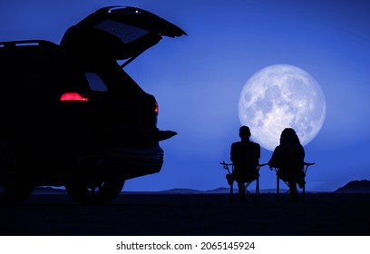 Couple Seating Next To Their Car And Enjoying Full Moon Vista During Scenic Desert Night. Outdoors Pursuit Theme