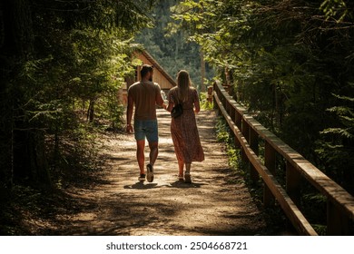 A couple, seen from behind, walks along a sunlit forest path next to a wooden cabin. The woman wears a floral dress, and the man is dressed casually in shorts and a t-shirt. The scene is serene and pe - Powered by Shutterstock