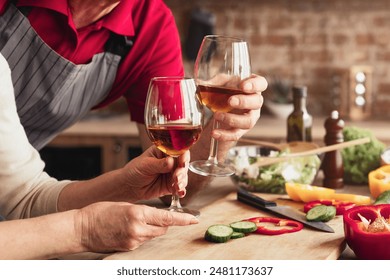 A couple is seen enjoying a glass of wine after preparing a meal in their kitchen. They are both smiling and enjoying each others company. The kitchen counter is cluttered with ingredients - Powered by Shutterstock