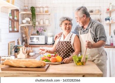 Couple Senior Asian Elder Happy Living In Home Kitchen. Grandfather Cooking Salad Dish With Grandmother With Happiness And Smile Enjoy Retirement Life Together. Older People Relationship And Activity.