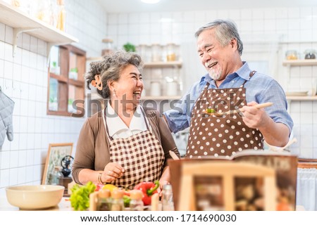 Couple senior Asian elder happy living in home kitchen. Grandfather cooking salad dish with grandmother with happiness and smile enjoy retirement life together. Older people relationship and lifestyle