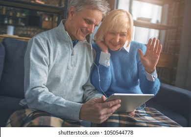 A Couple Of Senior People Are Speaking With Their Kids Using Skype Program On The Tablet. She Is Waving To Her Daughter On The Screen.