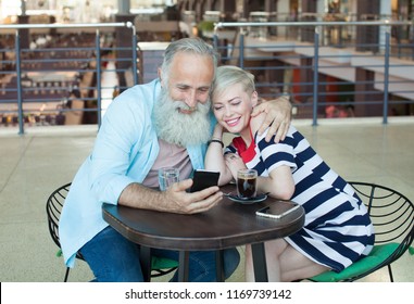 A Couple Of Senior People Are Speaking With Their Kids Using Skype Program On The Phone. She Is Waving To Her Daughter On The Screen.