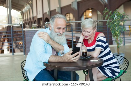 A Couple Of Senior People Are Speaking With Their Kids Using Skype Program On The Phone. She Is Waving To Her Daughter On The Screen.