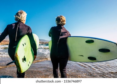 couple of seniors at the beach with black wetsuits holding a surftable ready to go surfing a the beach - active mature and retired people doing happy activity together in their vacations or freetime - Powered by Shutterstock