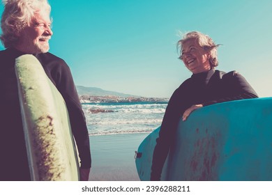 couple of seniors at the beach with black wetsuits holding a surftable ready to go surfing a the beach - active mature and retired people doing happy activity together in their vacations or freetime - Powered by Shutterstock