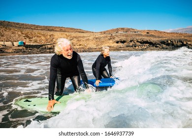 couple of seniors going surfing together - two mature people in the beach with surfboards and wetsuits looking at the sea entring in the water - learning surf - Powered by Shutterstock