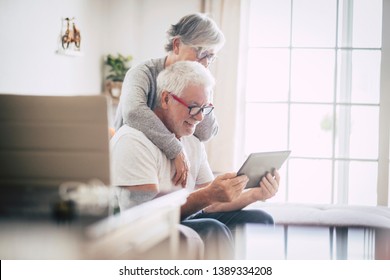 couple of seniors smiling and looking at the same tablet hugged on the sofa - indoor, at home concept - caucasians mature and retired man and woman using technology - lockdown and quarantine lifestyle - Shutterstock ID 1389334208