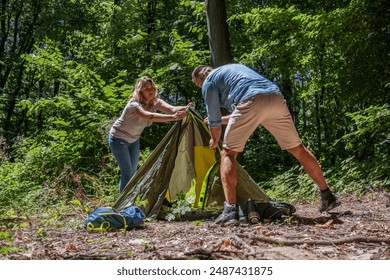 A couple sets up a tent together in nature on a sunny summer day. They work as a team, helping each other to prepare their campsite. - Powered by Shutterstock