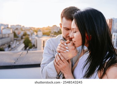 Couple sharing intimate moment on rooftop as sun sets behind city skyline. Man and woman embrace with hands clasped, affection and connection. Calmness of evening setting enhances romantic atmosphere. - Powered by Shutterstock