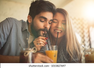 Couple Sharing Orange Juice In Cafe.