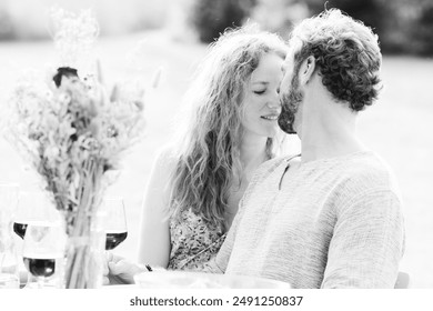 A couple is sharing a romantic moment at an outdoor dining setup with flowers and wine glasses present - Powered by Shutterstock