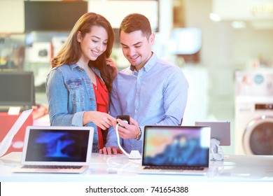 Couple Shopping For Latest Laptop And Smartphone At Tech Store